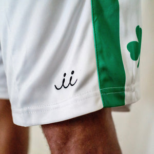 Chi Chi Sport white basketball shorts with green side stripe, shamrock detail, and embroidered logo on the leg.